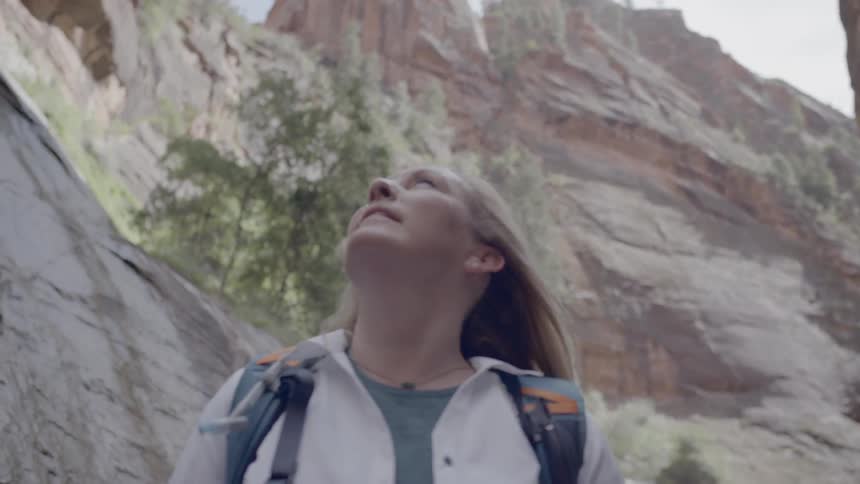 Blonde woman wearing backpack looks around in a valley between the two mountains