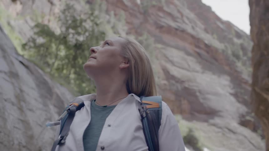 A woman with a backpack standing looking up with a cliff in the background