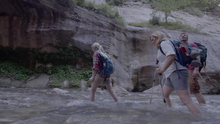 Hikers carefully walk through a flowing river in a canyon