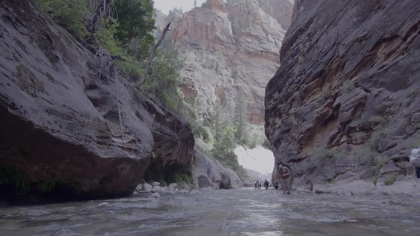 A group of people walk along a stream between two mountains