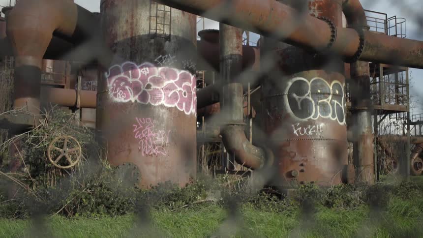 Old and rusted tanks and pipes of a factory as seen through a chainlink fence
