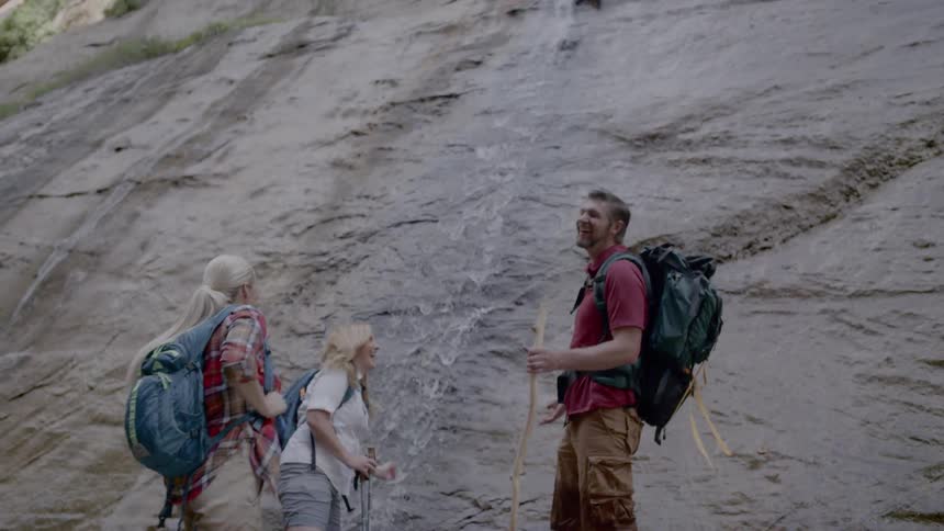 Three hikers stop at the bottom of a cliff to play in the water
