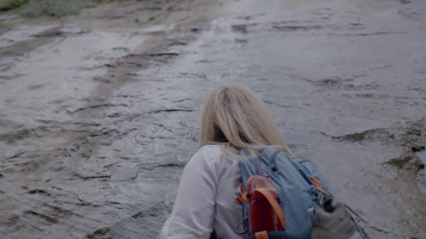 A woman looks up the mountain cliff with a stream of water running down