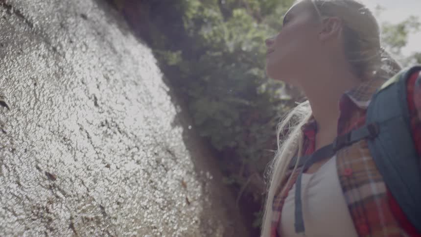 Young woman on a hike touches the side of a cliff