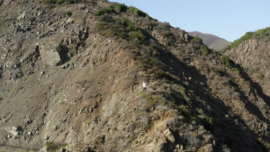Person standing on low ridge watches predatory bird fly over mountain