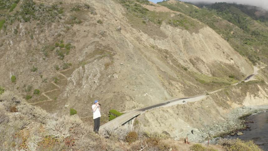 A man is taking pictures of the sea from a hill on the coast
