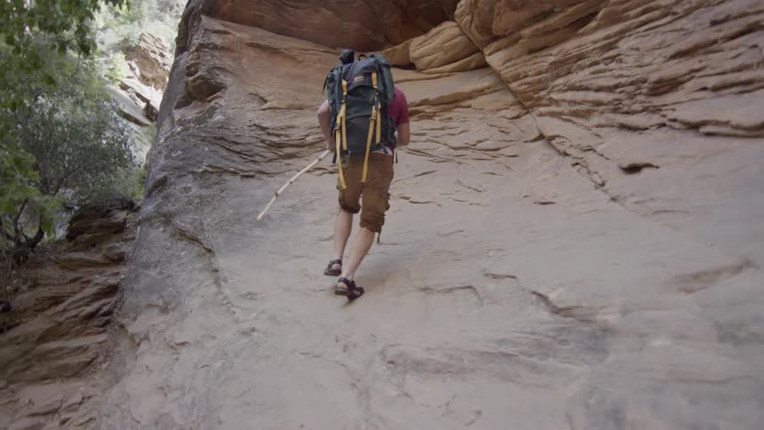 A hiker with a large backpack climbs on a rock in the wilderness