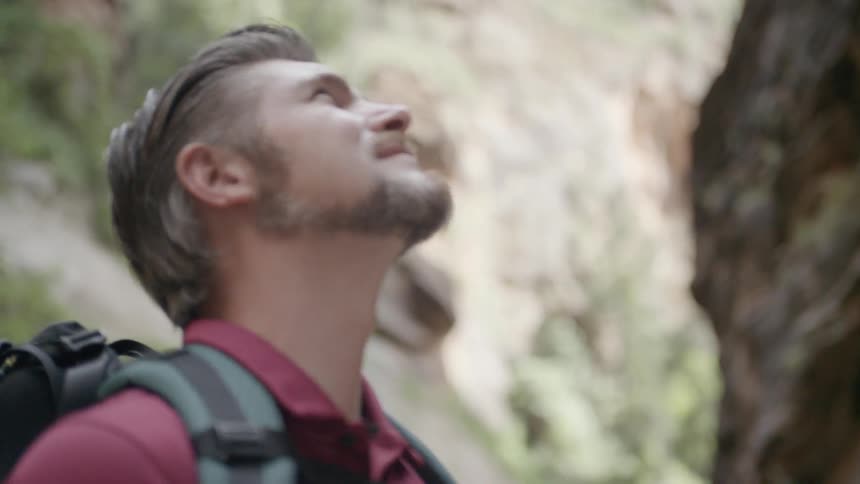 A man wearing a backpack looks upwards at the tower cliffs from where he stands in the canyon below