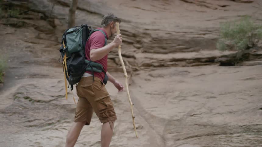 A man uses a walking stick to hike on the rocks next to water