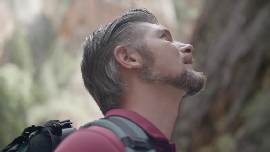 A man standing in a canyon is looking upward while carrying a backpack