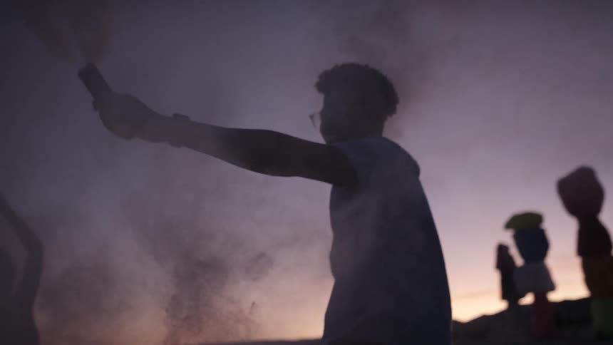 People dancing with flares at sunset next to art installations