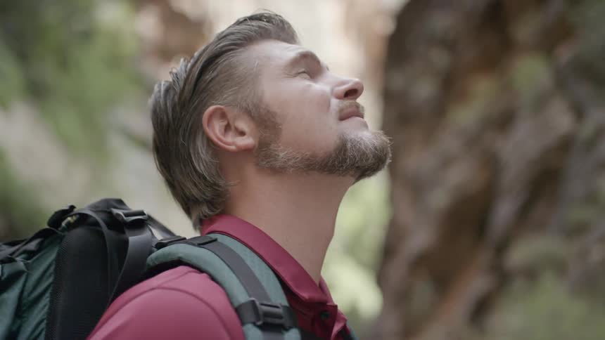Man wearing backpack looks up toward top of cliff