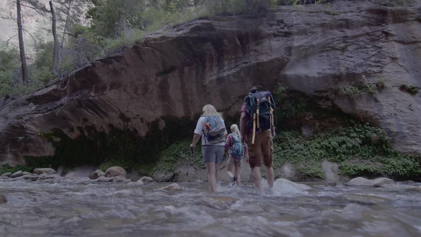 A white family hikes across a shallow stream
