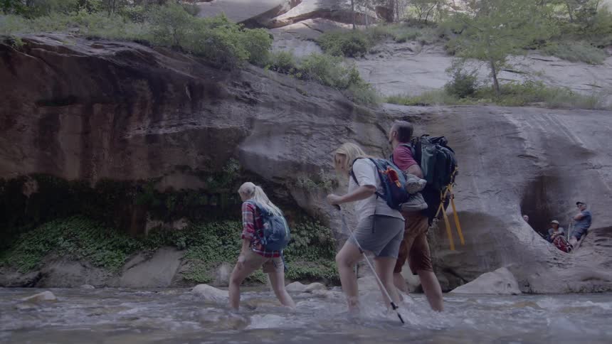 Group of friends hiking while crossing a shallow river on foot