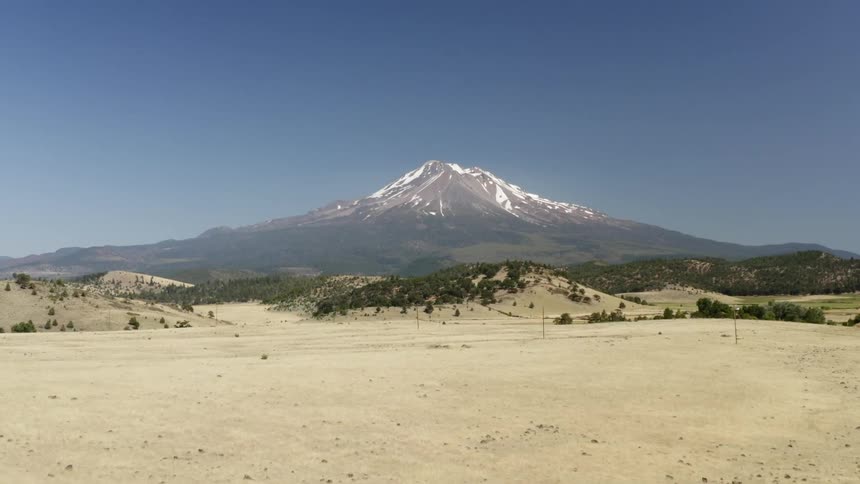 An enormous mountain that is topped with snow towers high above the dry and dusty landscape below