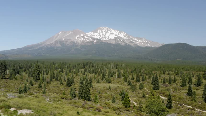 A snow covered mountain rises above a lightly forested valley