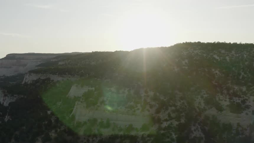 A range of plateaus is covered in sparse forests a the sun sits low in the sky above
