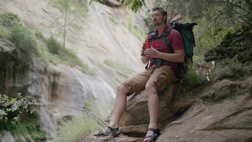 A man sits on rock and takes a drink of water