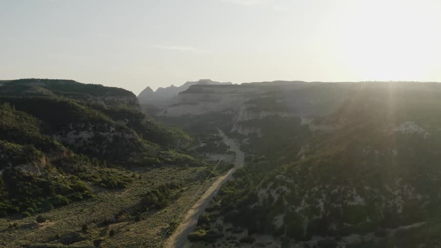 An aerial view of vegetation and a road in a canyon at dusk or dawn