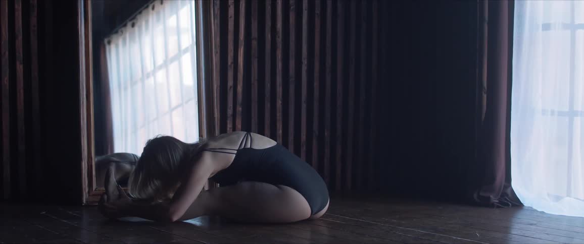 A woman in a leotard bends forward in a stretch in front of a mirror
