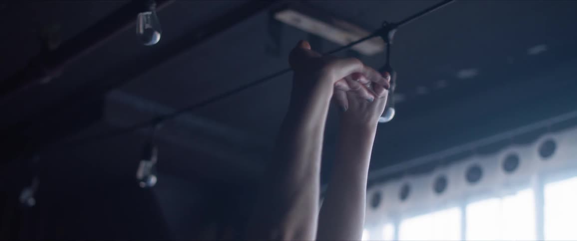 A white female dancer stretches in a dark room