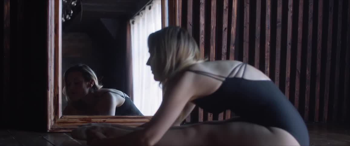 A woman in a leotard checking her form in a mirror as she does stretches on the floor