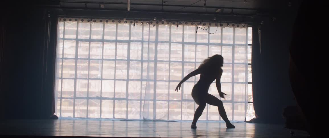 A ballerina dancing before a large window in a dark room