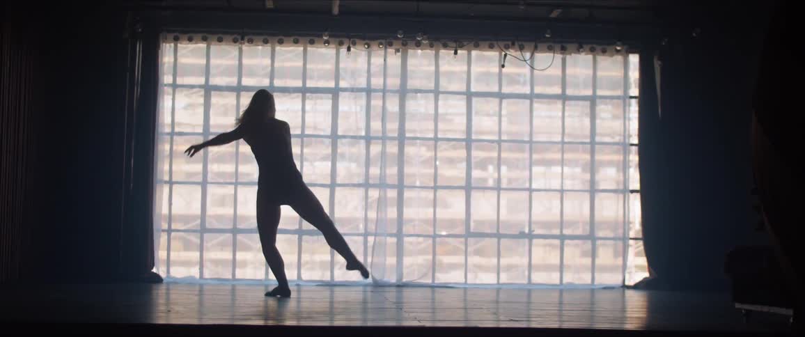 A woman is dancing indoors in front of a large studio window