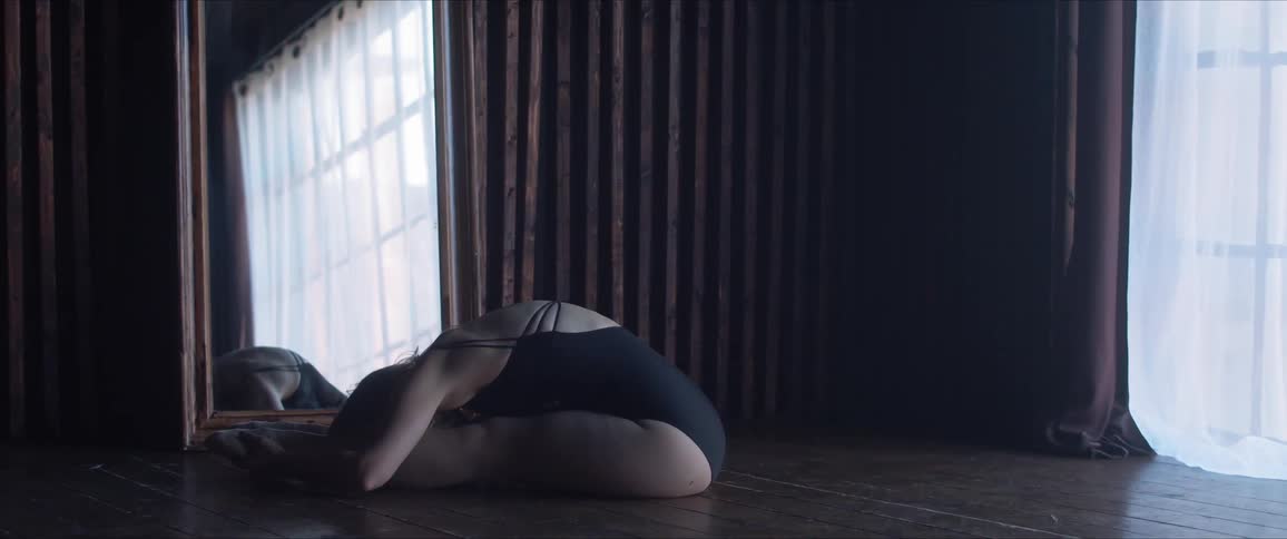 A woman in a bodysuit does stretches in front of a window