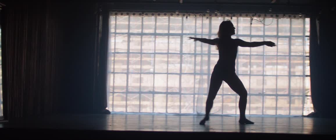 A woman dances in a dark room against a light window