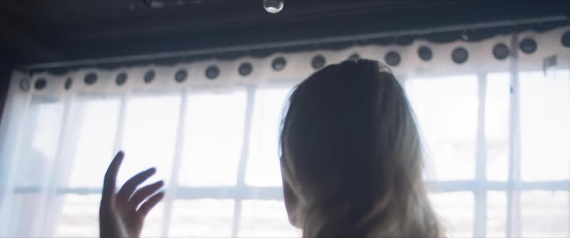 A young woman dancer lowers her arms in front of the window