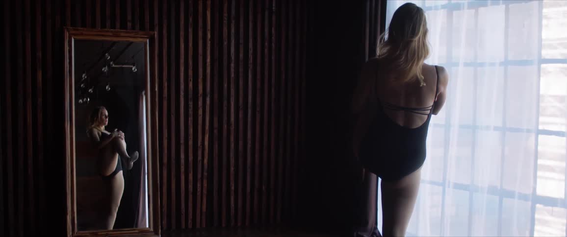 A woman in a bodysuit does stretches in front of a window