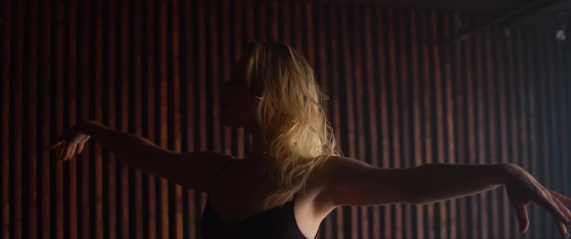 A blonde woman dances gracefully in a dark room