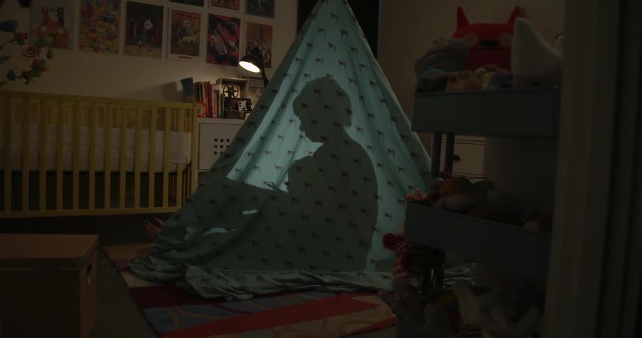 The silhouette of mother and child reading under a sheet