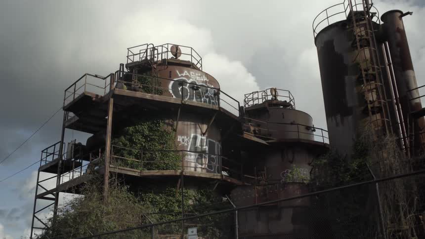 A group of rusty industrial buildings covered in graffiti on a cloudy day