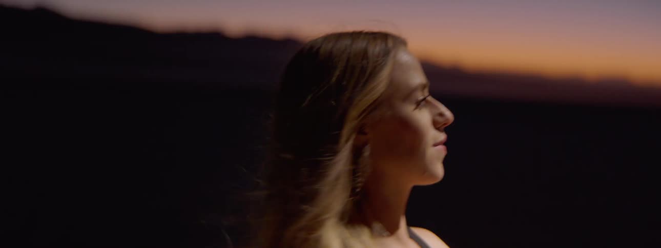 Man in suit and blonde woman dance in the spotlight outdoors at dusk