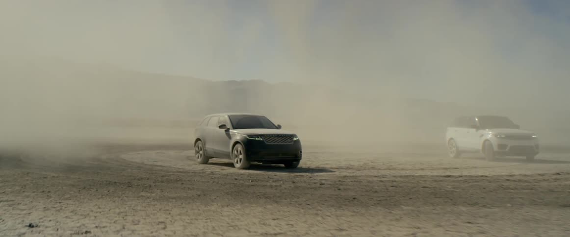 Dust blows around two sport utility vehicles parked in the desert