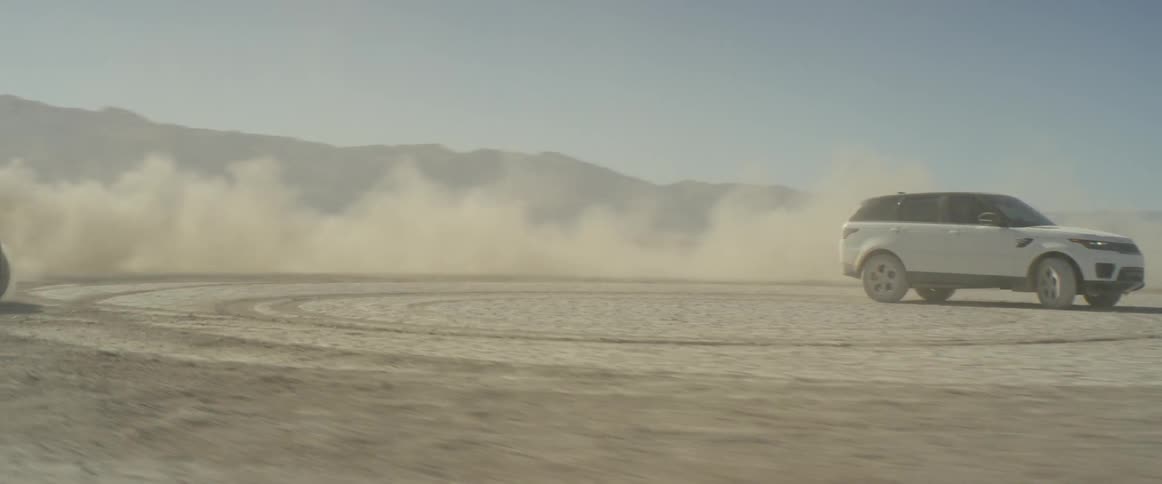 Two sport utility vehiclesare driving in circles and kicking up a cloud of dust on a dried lake bed