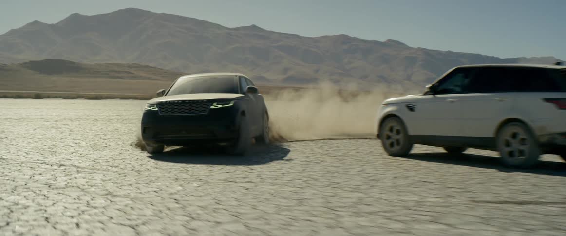 A motor vehicle drives in a circle around a stationary vehicle in the desert