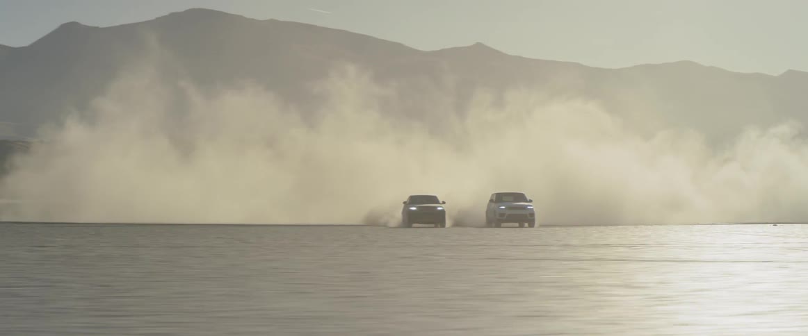 Two vehicles racing in the desert with mountains and the sky in the background
