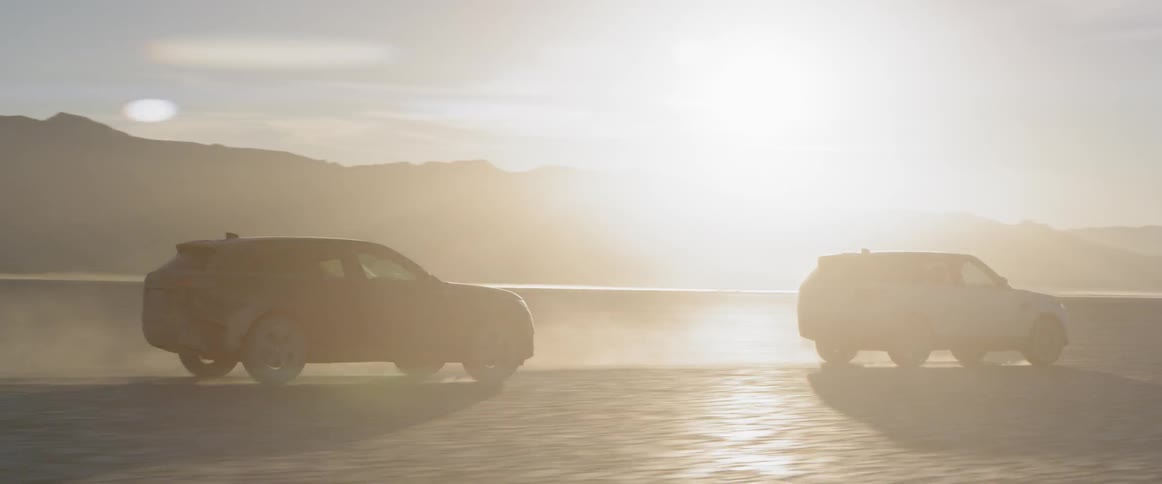 A black suv follows a white suv driving across the salt flats