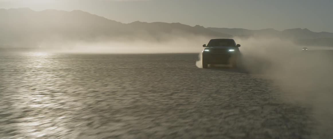 A car speeds past in the desert with mountains and the sky in the background