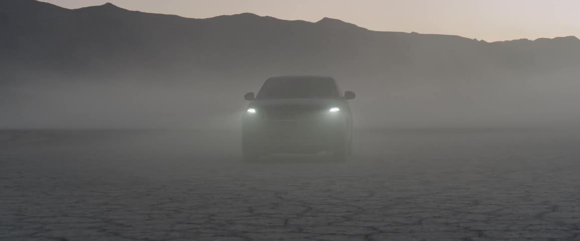 The car turns its headlights on at dawn in the desert