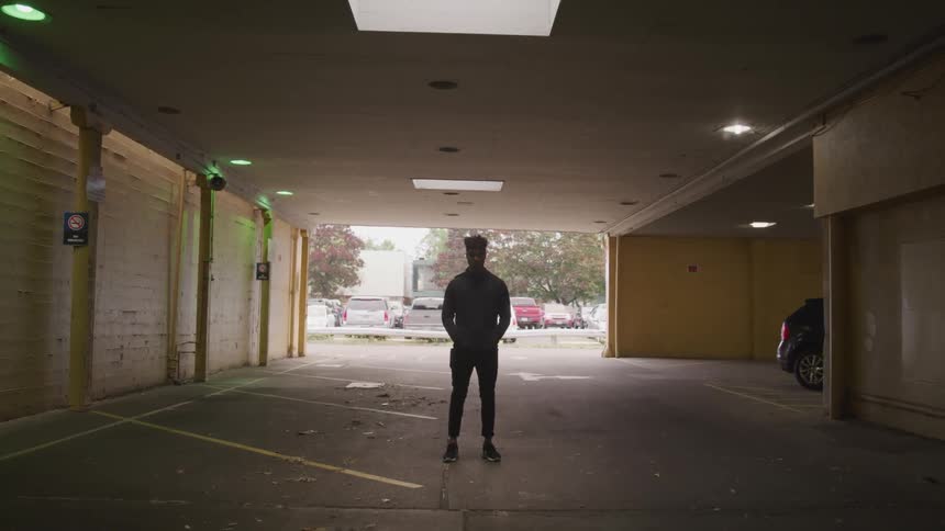 A man stands in a parking garage with his hands in his pocket