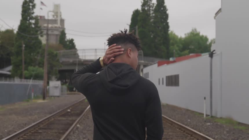 A young black man walking along train tracks