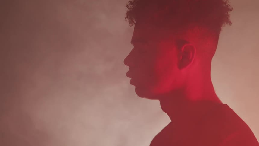 Man with eyes closed under red light surrounded by mist