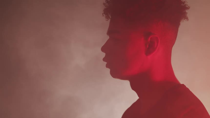 A black teenager stands and looks off in to the distance as smoke billows around him