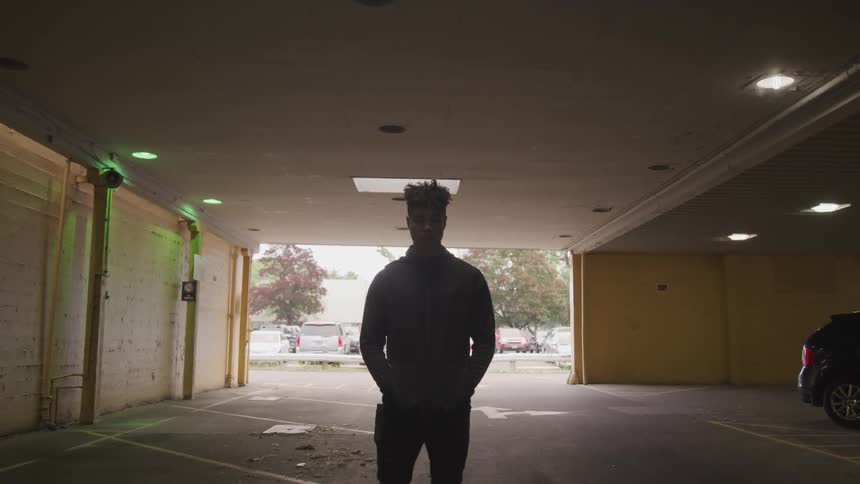 A black teenager stands in a parking garage