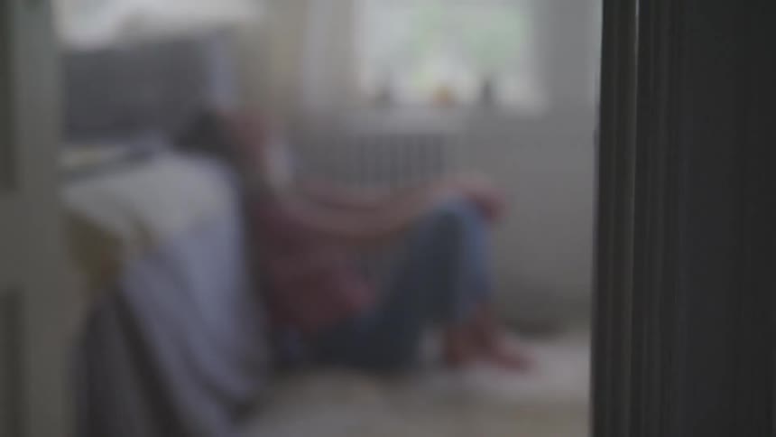 A young female sits in a bedroom floor and relines against the sit of the bed