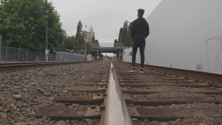 A young black man walks down train tracks